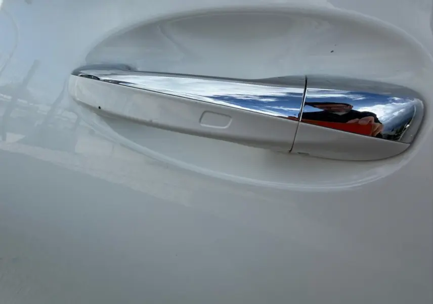 Gros plan sur la poignée de porte chromée côté droit d’une Mercedes Classe A 220D AMG Line blanche.