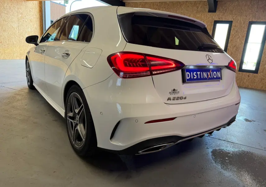 Vue 3/4 arrière droite d'une Mercedes Classe A 220d AMG Line blanche avec feux arrière allumés en intérieur.