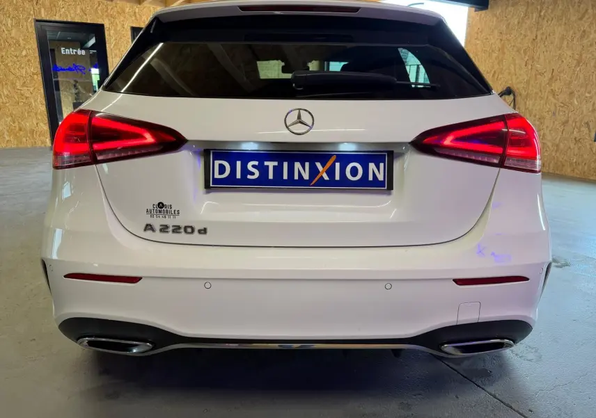 Vue arrière d'une Mercedes Classe A 220d AMG Line blanche avec feux arrière allumés et double sortie d'échappement chromée.