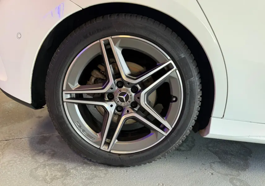 Gros plan sur la roue arrière droite d’une Mercedes Classe A 220D AMG Line blanche, avec jante alliage cinq branches.