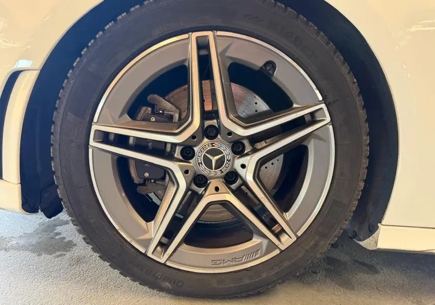 Gros plan sur la jante AMG en alliage gris avec logo Mercedes, montée sur une Mercedes Classe A blanche côté gauche.