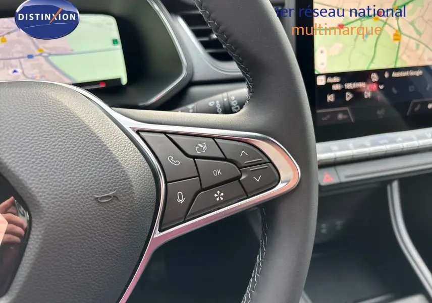 Gros plan sur le volant côté droit du Renault Captur II hybride 2025, avec commandes intégrées et écran tactile en arrière-plan.