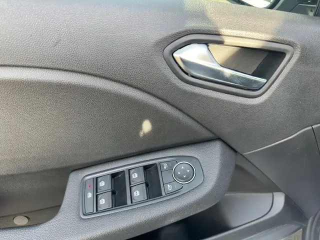 Gros plan sur la porte côté conducteur de la Renault Clio V blanche, montrant les commandes des vitres électriques et la poignée intérieure grise.