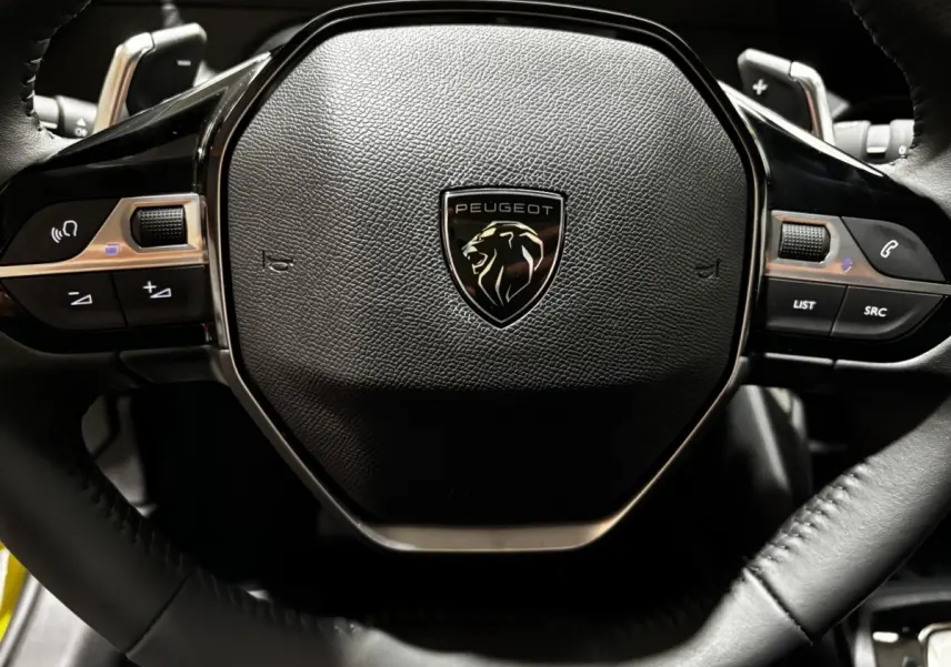 Gros plan sur le volant noir de la Peugeot 208 Hybrid 110 e-DCS6 Style avec logo lion central.