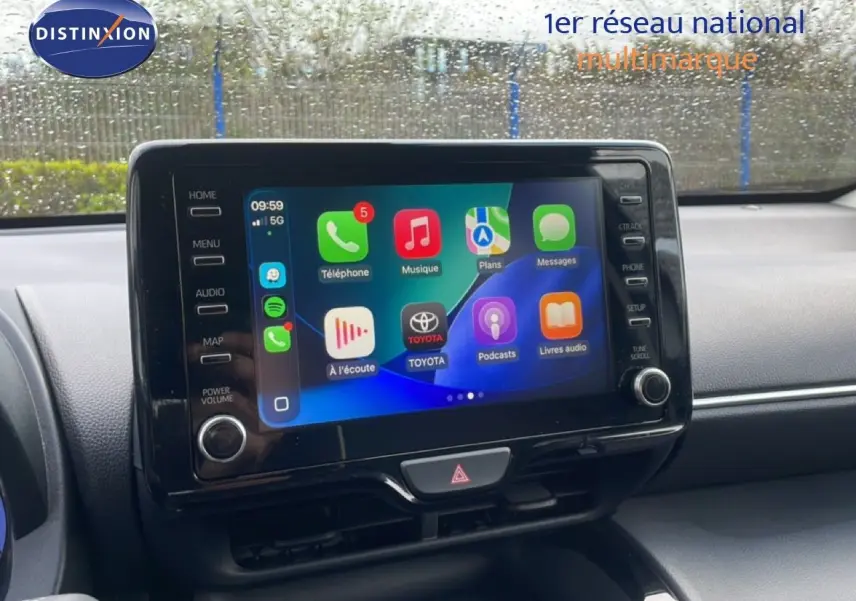 Écran tactile central allumé dans l’habitacle d’une Toyota Yaris Cross blanche, vue de face sous la pluie.