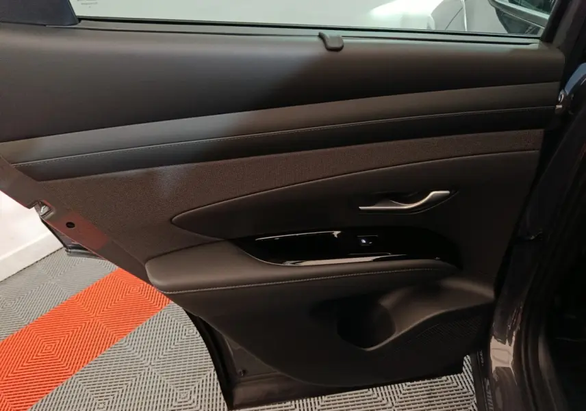 Vue intérieure de la porte arrière gauche du Hyundai Tucson gris foncé, avec garniture tissu et cuir et poignée argentée.