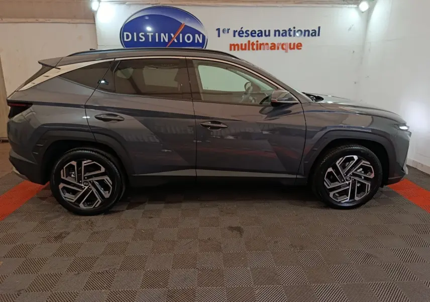 Vue de profil côté gauche d'un Hyundai Tucson gris foncé avec jantes alliage au design moderne, en intérieur showroom.