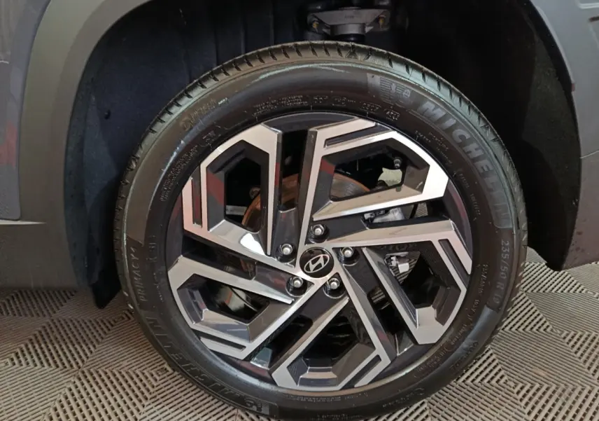 Gros plan sur la roue avant droite du Hyundai Tucson gris foncé, mettant en valeur la jante alliage au design géométrique.