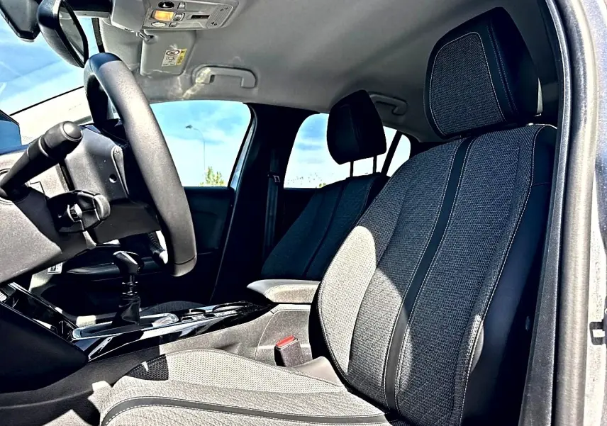 Vue intérieure côté conducteur de la Peugeot 208 1.2 100 allure avec sièges tissu gris et volant noir.