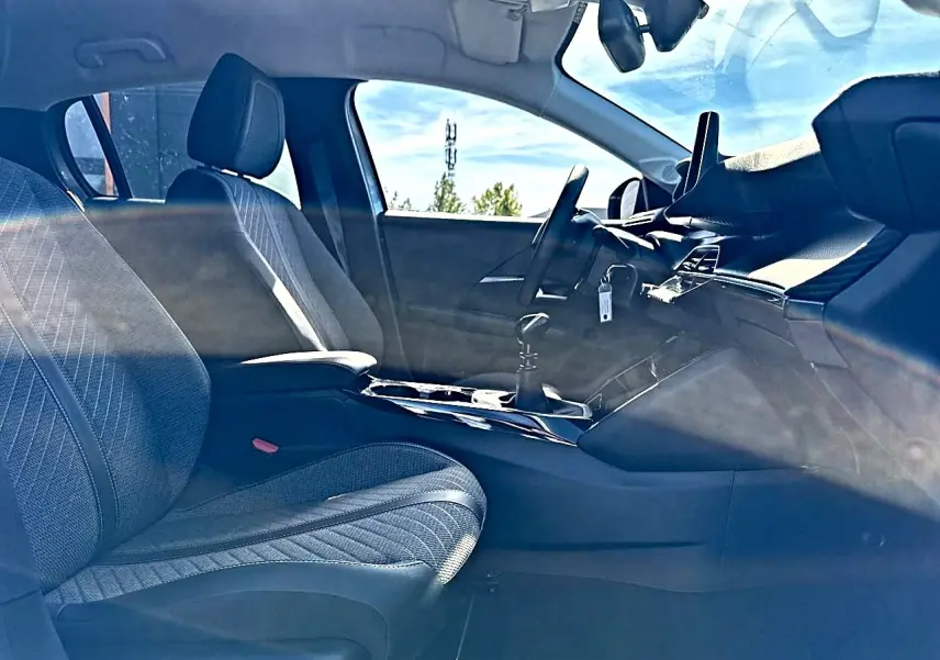 Vue intérieure côté conducteur de la Peugeot 208 1.2 100 Allure 2025, sièges tissu gris et tableau de bord moderne.