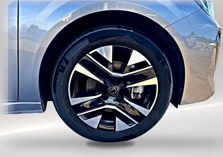 Gros plan sur la roue avant droite avec jante alu bicolore d'une Peugeot 208 gris artense, partie de la carrosserie visible.