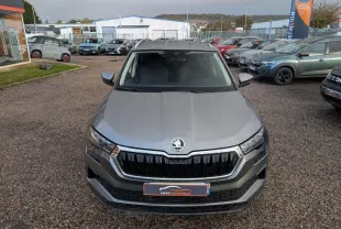 Vue avant d'un Skoda Karoq gris métallisé 2024 avec calandre noire et logo centré, stationné en extérieur sur un parking.