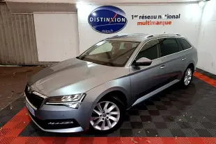Vue 3/4 avant droite d'une Skoda Superb gris clair en break, stationnée en intérieur sur sol noir et rouge.