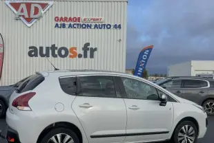 Peugeot 3008 blanc vue de profil côté gauche, stationné devant un garage avec logo autos.fr visible.