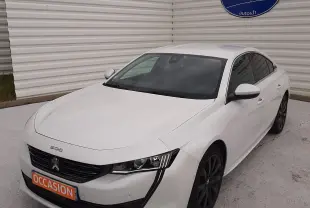 Peugeot 508 blanche vue en 3/4 avant droit, avec calandre noire et jantes foncées, stationnée devant un mur blanc.