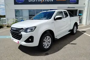Vue de profil côté droit d'un pick-up Isuzu D-MAX blanc avec arceau noir et couvre-benne roulant, stationné devant un bâtiment industriel.