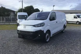 Fourgon FIAT Scudo blanc en 3/4 avant droit, avec pare-chocs noir et jantes acier, stationné sur un sol gravillonné.