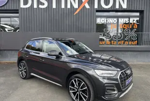 Audi Q5 gris en vue 3/4 avant droit, avec jantes alliage noires et calandre chromée, stationné devant un mur noir.