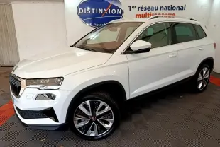 Vue 3/4 avant droite d'un Skoda Karoq blanc 2023 avec jantes alliage et barres de toit chromées.