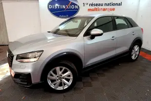 Audi Q2 35 TDI gris clair vue 3/4 avant droit en intérieur avec jantes alliage et phares allumés.