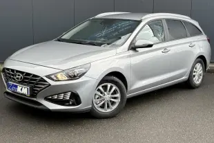 Hyundai i30 SW T-GDI 120 gris argent en 3/4 avant droit, avec jantes alliage et feux allumés.