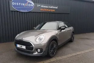 MINI Clubman F54 Silver Metal en 3/4 avant droit, toit noir et jantes foncées sur parking devant un mur noir.