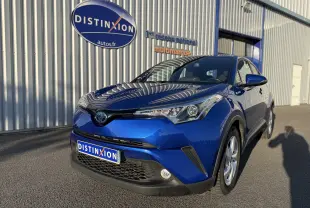 Toyota C-HR bleu Nebula Metal en 3/4 avant droit, avec calandre noire et phares anguleux, stationné devant un bâtiment.