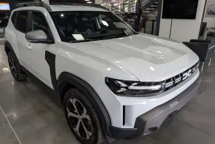 Vue 3/4 avant droite du Dacia Duster Hybrid-G blanc Glacier avec détails noirs contrastants et jantes bi-ton en showroom.