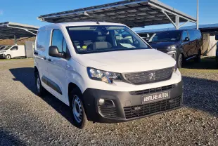 Vue 3/4 avant d'un Peugeot Partner blanc 2021 avec pare-chocs noir et plaque Abeilhe Autos sur un parking extérieur.