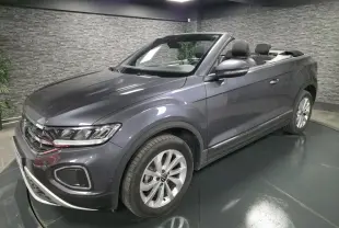 Volkswagen T-Roc cabriolet gris métallisé vu de 3/4 avant droit avec capote ouverte en intérieur showroom.