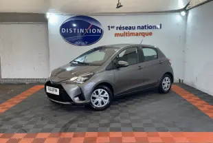 Toyota Yaris gris foncé vue 3/4 avant droit dans un showroom avec sol à damier noir et orange.