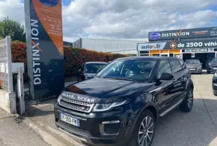 Range Rover Evoque 2015 noir en 3/4 avant droit, garé devant un concessionnaire Distinxion sous un ciel nuageux.