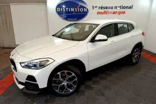 BMW X2 blanc en 3/4 avant droit dans un showroom, mettant en valeur ses phares LED et jantes design.