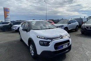 Citroën C3 blanc vue 3/4 avant droit, avec calandre noire et enjoliveurs 15 pouces sur parking extérieur.