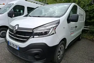 Renault Trafic Fourgon blanc vu en 3/4 avant droit avec marquage commercial sur la porte latérale droite.