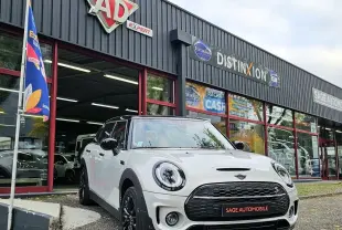 Vue 3/4 avant d'une MINI Cooper S Clubman blanche avec toit noir, garée devant un garage Sage Automobile.