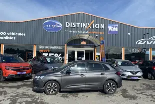 Profil côté gauche d'une Citroën C4 gris platinium 2017 garée devant un concessionnaire multimarque.