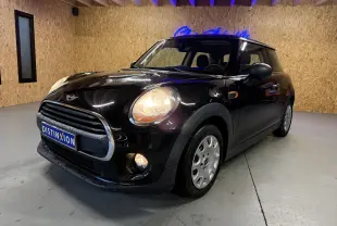 Mini One noire vue 3/4 avant droit en intérieur, phares et antibrouillards allumés, calandre chromée visible.