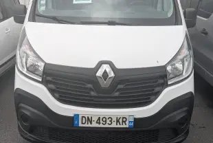 Vue frontale d'un Renault Trafic blanc avec calandre noire et double portes arrière, stationné entre deux véhicules.
