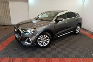 Audi Q3 Sportback gris clair en 3/4 avant droit, avec jantes alliage et prise de recharge visible côté avant gauche.