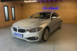 BMW Série 4 Cabriolet gris vue 3/4 avant droit dans un showroom avec éclairage intérieur et logo néon bleu.
