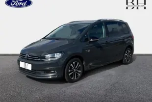 Volkswagen Touran gris Urano en 3/4 avant droit, avec jantes alliage et barres de toit visibles.