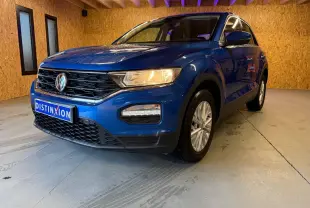 Volkswagen T-Roc bleu en 3/4 avant droit, avec phares allumés et calandre noire distinctive.