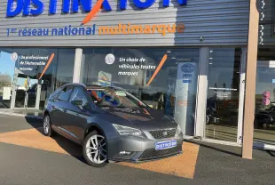 SEAT LEON ST gris en 3/4 avant droit, stationnée devant un showroom avec plaques Distinxion visibles.