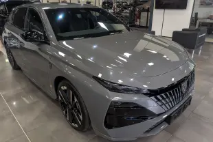 Peugeot 308 gris Sélénium vue 3/4 avant droit en showroom, avec calandre noire distinctive et jantes bicolores.