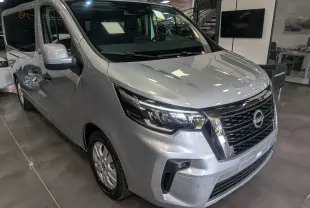 Vue 3/4 avant droite du Nissan Primastar Combi gris Highland 2026 avec calandre noire et phares LED distinctifs.