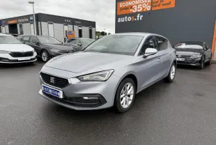 SEAT Leon 2.0 TDI 2022 en gris argenté, vue 3/4 avant droit sur parking devant un bâtiment commercial.