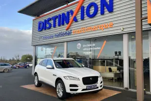 Jaguar F-PACE blanc en 3/4 avant droit, stationné devant un showroom Distinxion avec une calandre noire distinctive.