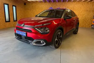 Citroën C4 X rouge vue 3/4 avant droit dans un garage avec éclairage intérieur et jantes noires.