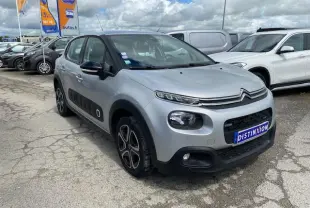 Citroën C3 gris clair vue 3/4 avant droit avec enjoliveurs 3D et protections latérales noires sur parking.